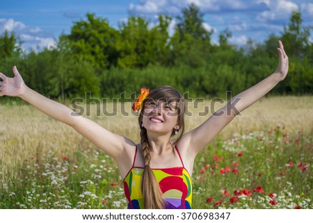 Beautiful young woman with a braid in a field of poppies in the morning pulls hands to the sun. Young girl enjoys the sun. Rejoice good weather. Joy nature