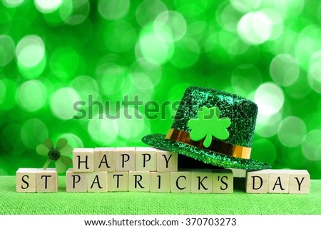 Happy St Patricks Day wooden blocks with leprechaun hat and shamrock over twinkling green background