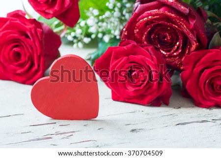 A bouquet of roses on a wooden table with a red heart.