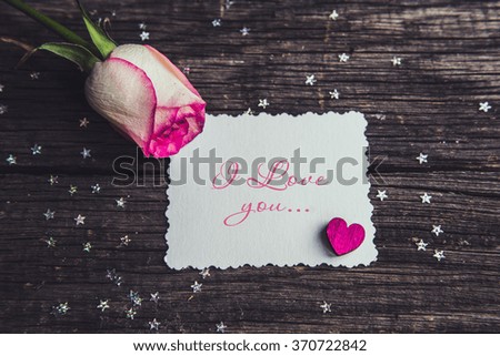 Pink roses with a note declarations of love. On a wooden board