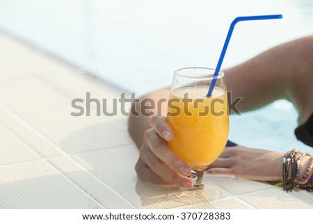 Beautiful blond enjoying on a swimming pool, drinking an orange juice