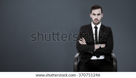 Serious businessman sitting with arms crossed against grey background