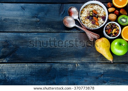 Dark rustic table with healthy breakfast. Oat flakes with pumpkin seeds, nuts, dry berries and fresh fruits on vintage wooden background. Top view. Royalty-Free Stock Photo #370773878