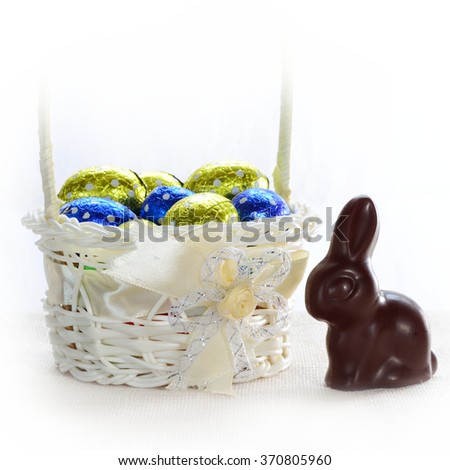 Easter chocolate bunny and a full basket of blue and yellow foiled chocolate eggs. Isolated on white