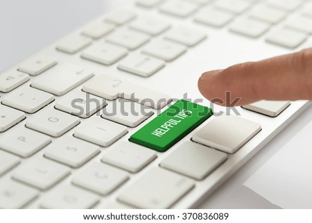 Computer Keyboard Concept: Hand pushing green HELPFUL TIPS keyboard button