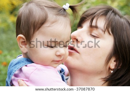 Happy mother kissing baby daughter outdoors