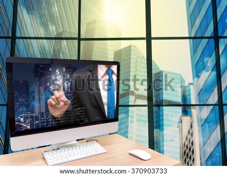 the computer on the wood table with Businessman point sign of money on the trading graph at the screen in front of the glass window over the blurred photo of cityscape background