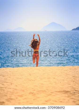 blonde slim girl in bikini runs with hands aside barefoot from sea on sand laughs wind shakes long hair
