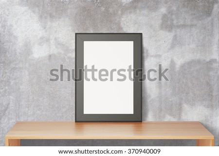 Blank black picture frame on wooden table and concrete wall, mock up