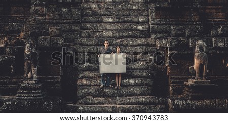 Young woman and man holding blank placard in dark mystic location