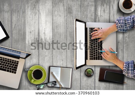 Top view of hands working with a laptop in a dark over wooden table.office supplies and gadgets on vintage table background.
