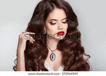 Beauty Makeup. Healthy hair. Beautiful girl with long wavy hairstyle. Brunette with luxury jewelry, red lips posing isolated on studio background. 
