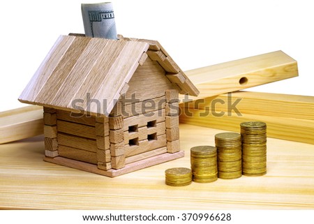 A small house standing at building materials and coins. Credit for the construction of wooden house in the mountains. Buying a new home. Isolated on white background.