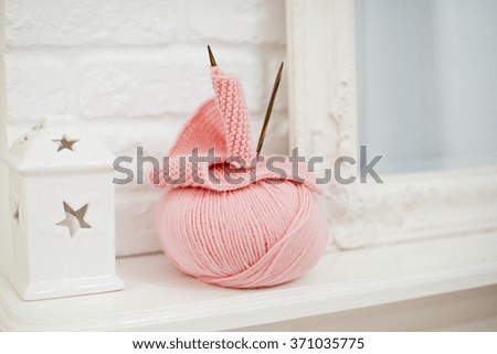 Cute pink knitting needles and yarn lying on the shelf near the mirror with white vintage frame