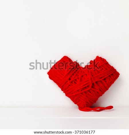 closeup of a heart-shaped coil of red yarn on a white surface against a white background