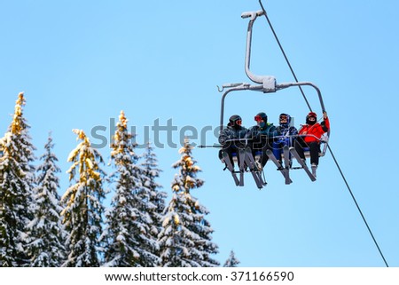 Bottom view of ski family on chair lift in vacation in the mountains. Father, mother and two children with skis and ski gear. Royalty-Free Stock Photo #371166590