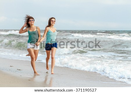 outdoor portrait of two young happy girls running on tropical sea background, holiday image