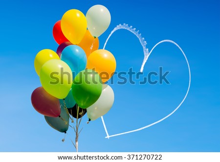 Colorful bunch of balloons and romantic heart written in the sky by an aircraft