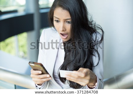 Closeup portrait, young woman in white gray suit looking at cell phone and paper, shocked at what she sees, isolated indoors background. Winning lottery ticket