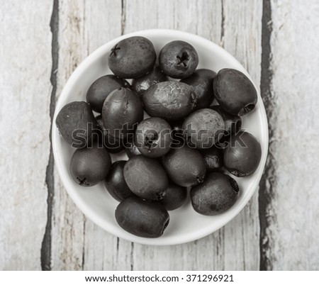 Pickled black olives fruit in white bowl over wooden background