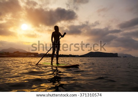 Silhouette of a beautiful woman on Stand Up Paddle Board. SUP. Royalty-Free Stock Photo #371310574