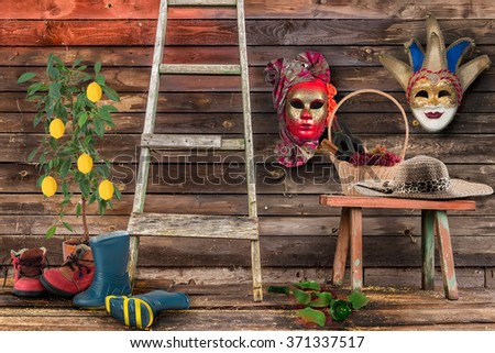 Two carnival masks hanging  wall  bottom  wooden bench  wicker basket bottles  wine  grapes straw hat  floor broken bottle staircase two pairs shoes men's women's  lemon tree  ceramic pot