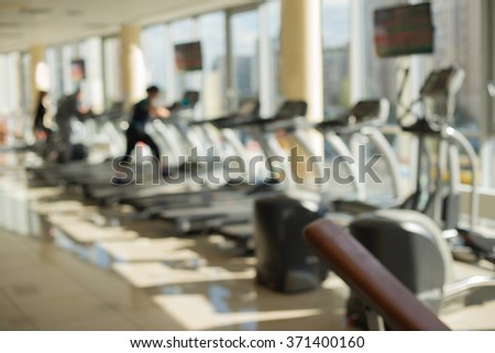 Training apparatus in gym. Blurred picture of gym. People are training on bikes and treadmills in gym.