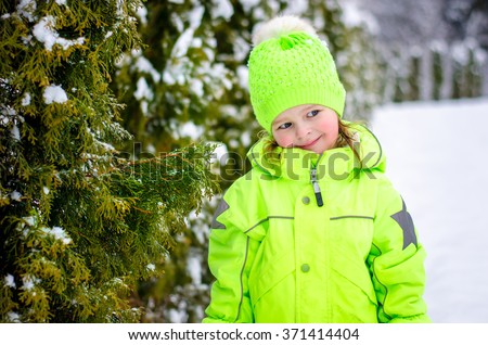 Little beautiful girl in a bright green winter clothes walking in a winter park.