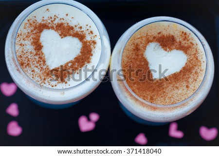 Close up two milk desserts with the image of heart on a black background