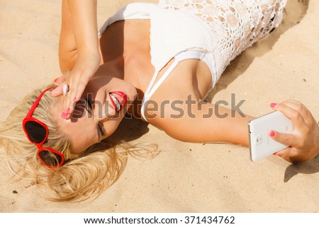 Technology and summer. Woman in red heart shaped sunglasses texting on mobile phone, using smartphone reading sms or taking photo of herself on beach