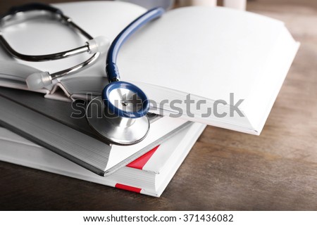 Stethoscope with stack of books on wooden background. Medical literature concept Royalty-Free Stock Photo #371436082