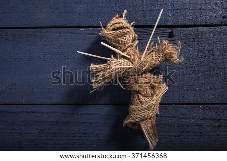 One cross shaped Halloween rag voodoo doll pierced with sticks on chest on blue wooden timber background, horizontal photo