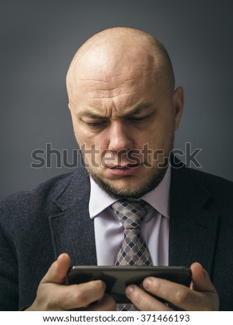 Portrait of an adult man in a business suit on a black background. Sad man almost in tears by what he sees on his cell phone, an sms, text message or email