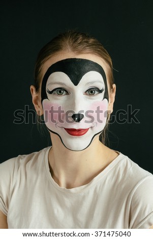 Smiling young woman with face painting mouse on black background