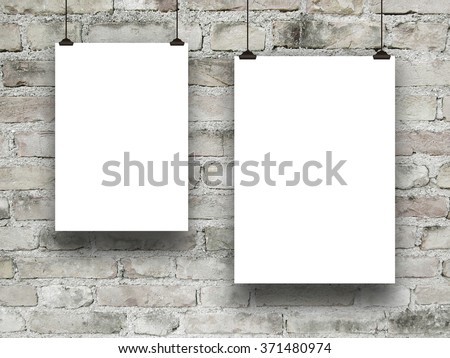 Close-up of two hanged asymmetrical paper sheets with clips on grey brick wall background