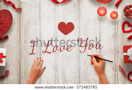 Girl hand painting I love you message on a wooden background. Love decorations beside, gifts, candles, hearts