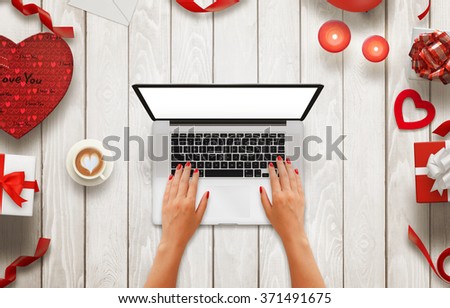 Girl work on laptop with isolated screen on a wooden background. Love decorations beside, coffee, gifts, candles, hearts