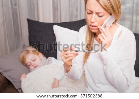 Mother calling doctor and looking at thermometer 