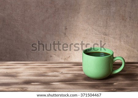 Coffee in cup on wooden table opposite a defocused burlap background.