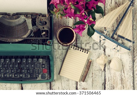 image of vintage typewriter, blank notebook, cup of coffee and old sailboat on wooden table