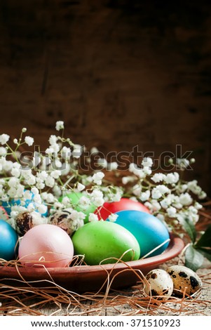 Multi-colored Easter eggs and quail eggs on a clay plate with white flowers, selective focus