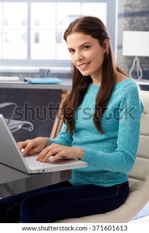 Young woman using laptop computer at home, smiling, looking at camera