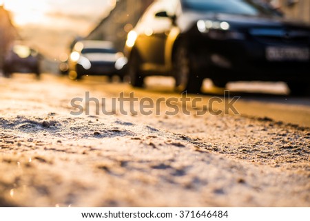 Bright winter sun in a big city, on the snowy street going cars. View from the road level