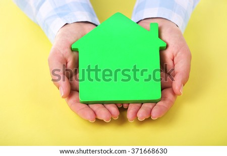 Female hands holding house on yellow background