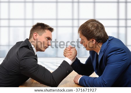 We are in a competitive business. Two businessmen arm wrestling. Modern office background.