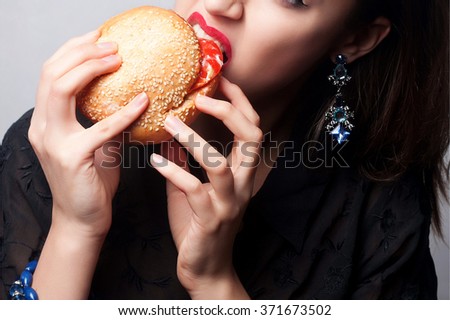 close-up portrait of a beautiful brunette girl eating a big hamburger. red lips , studio photo