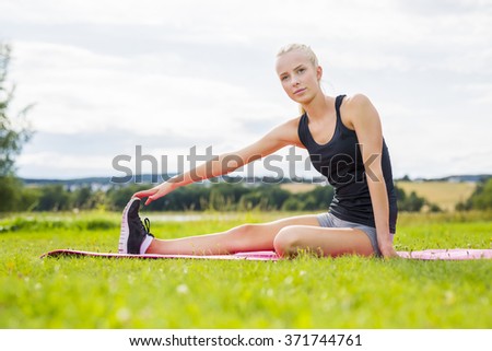Smiling blonde woman stretching outdoor on the grass