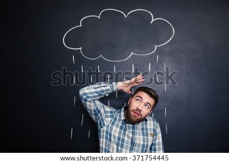 Unhappy young man hiding from raincloud and rain drawn over him on a blackboard background  Royalty-Free Stock Photo #371754445