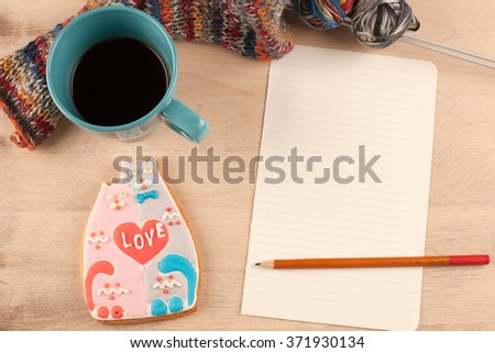 Women's hobby. Glazed cookies in the form of lovers of cats, a blank sheet of paper, a pencil, a Cup of coffee and an unfinished knitting on wooden background