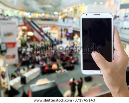 Man use mobile phone, blur image of event in the mall as background.